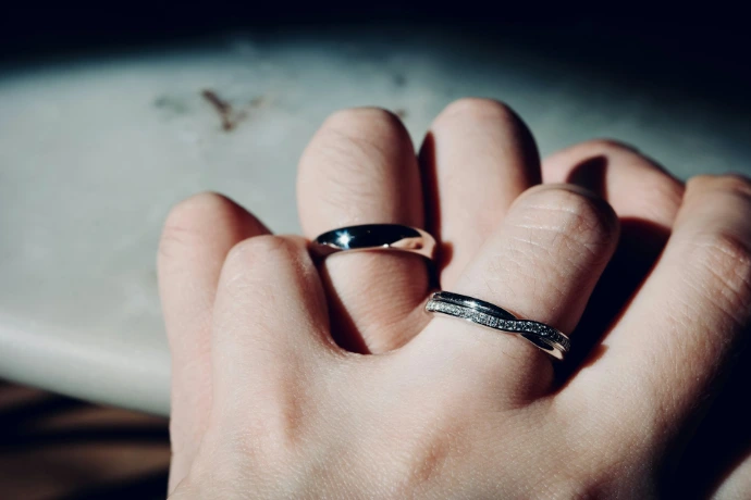 A hand wearing a plain silver band and a diamond-encrusted twisted ring